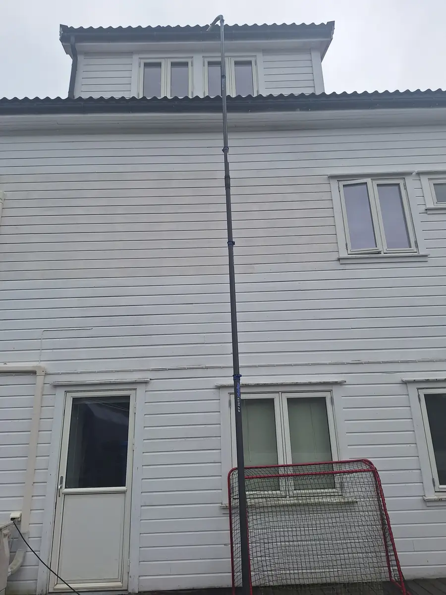 Stang fra SkyVac rekker opp til takrennen på et hvitt hus i tre etasjer